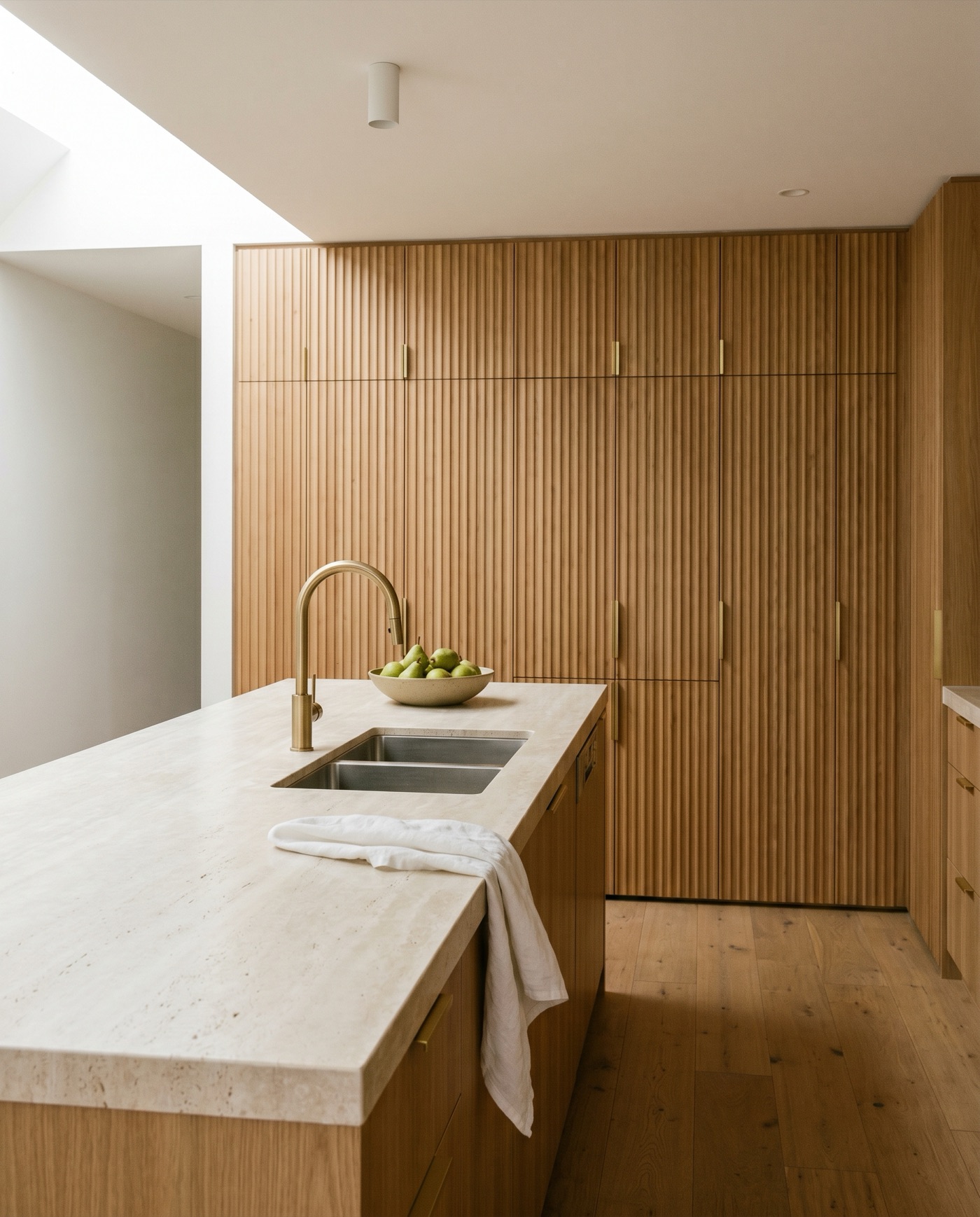 A finished premium Australian kitchen with a travertine-topped island, brushed-brass tapware and fluted oak cabinetry